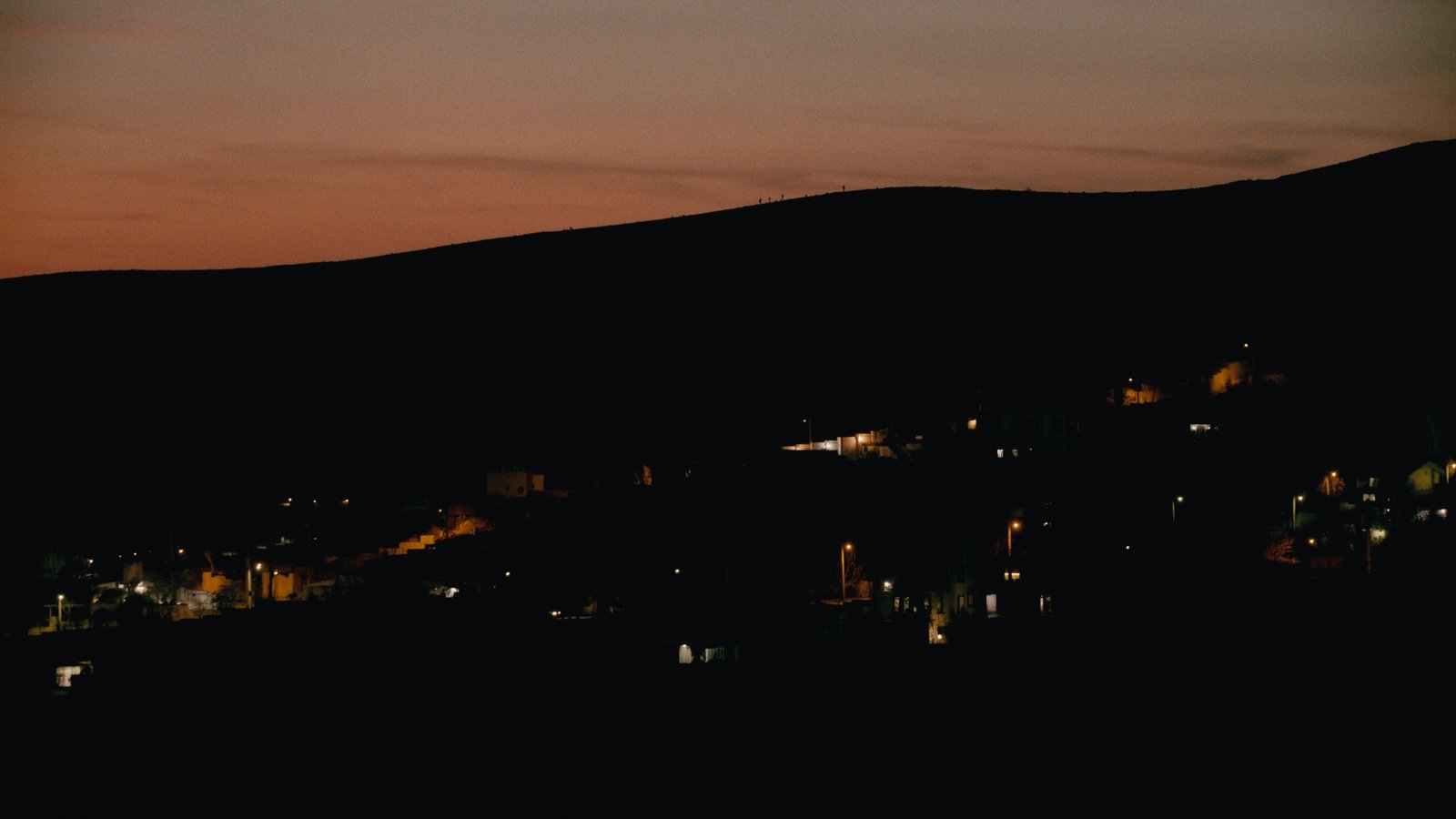 Hillside houses illuminated beneath a dusk sky in Passengers (2024).